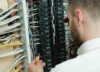Anchor Home Comfort electrical technician examining wiring connections inside a circuit breaker panel for a residential service check. Anchor Home Comfort electrical technician examining wiring connections inside a circuit breaker panel for a residential service check.