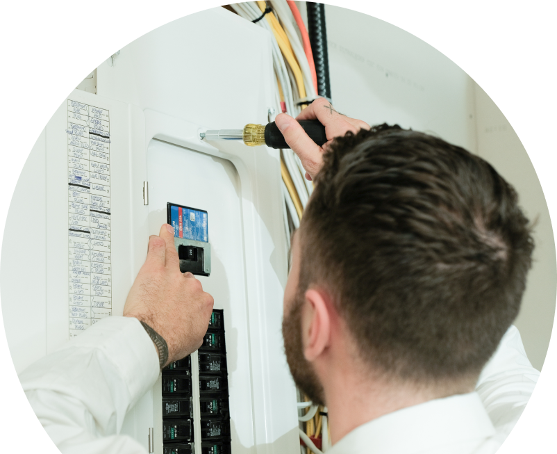 Anchor Home Comfort electrician using a screwdriver to perform an electrical panel upgrade, working near organized wiring in a residential wall. Anchor Home Comfort electrician using a screwdriver to perform an electrical panel upgrade, working near organized wiring in a residential wall.
