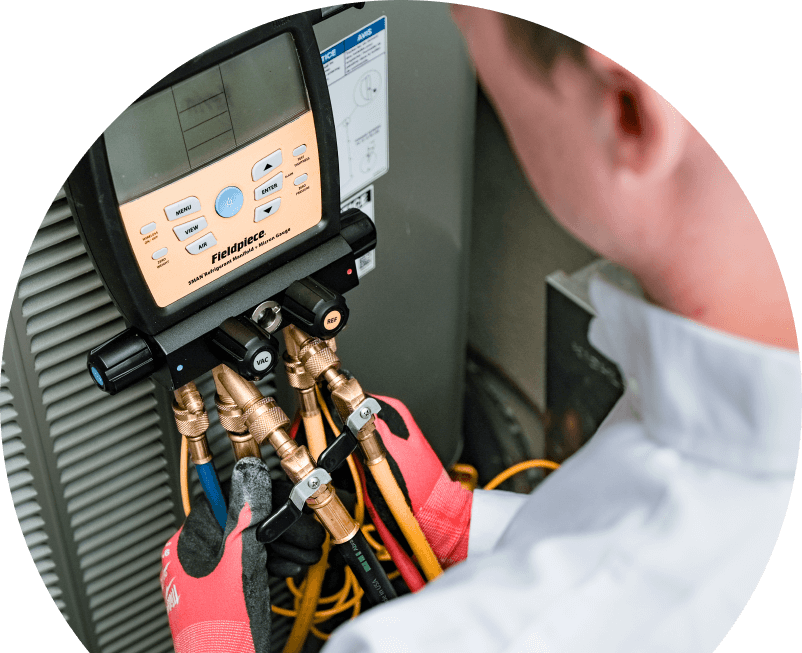 A Anchor Home Comfort home service crew member uses a digital manifold gauge to check refrigerant levels on an HVAC unit for service. A Anchor Home Comfort home service crew member uses a digital manifold gauge to check refrigerant levels on an HVAC unit for service.