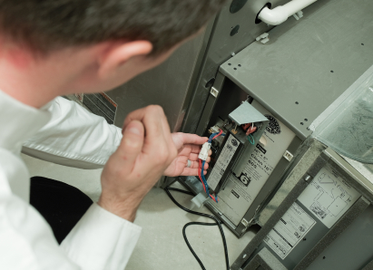 A Anchor Home Comfort heating technician inspecting internal wiring during a service check on a residential heating unit. A Anchor Home Comfort heating technician inspecting internal wiring during a service check on a residential heating unit.