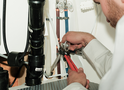 Using two pipe wrenches, a Anchor Home Comfort professional plumber services a pipe connection near a vertical flue or vent pipe. Using two pipe wrenches, a Anchor Home Comfort professional plumber services a pipe connection near a vertical flue or vent pipe.
